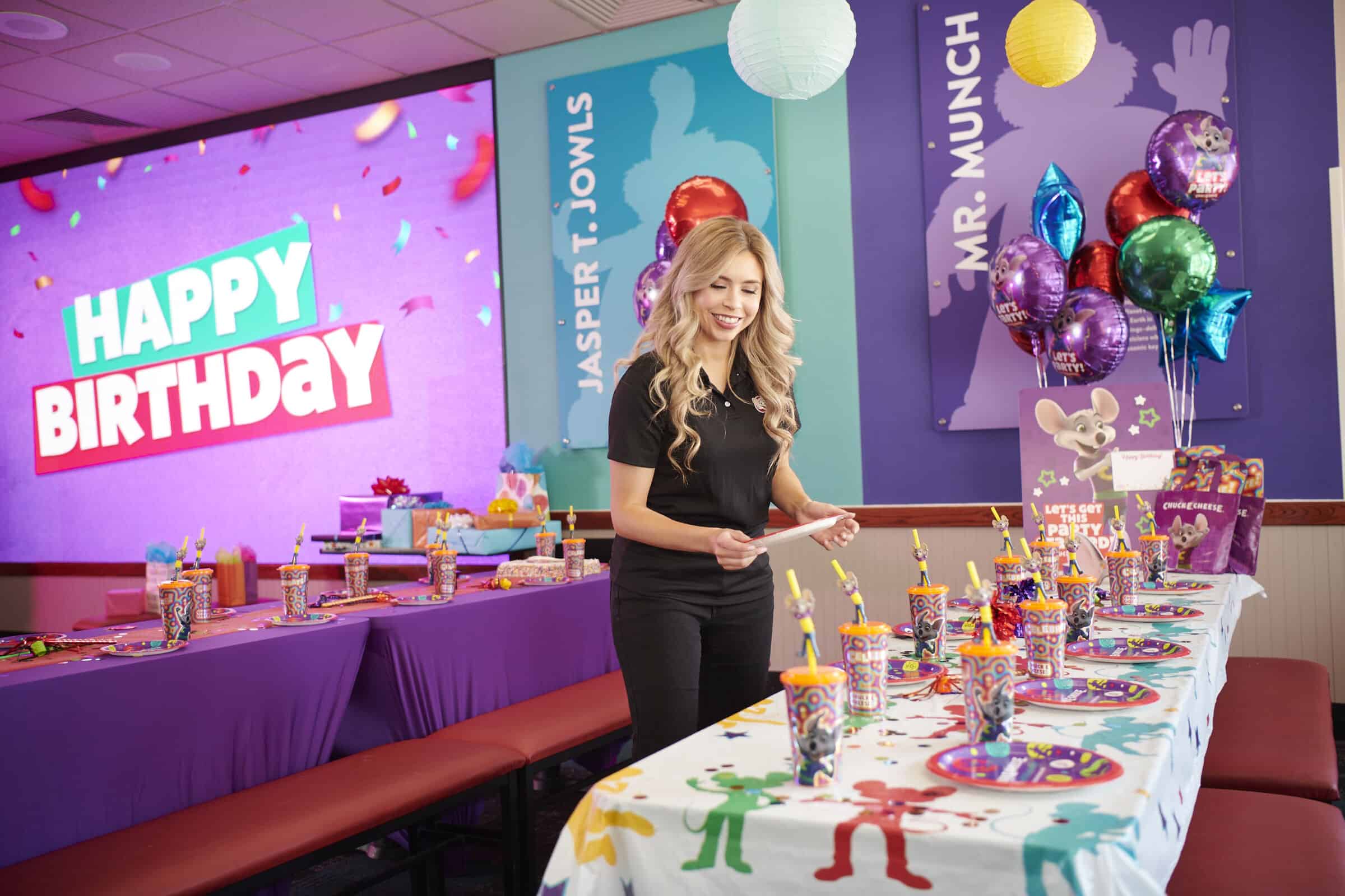 Birthday party table set with Happy Birthday screen, colorful decorations, and party favors at Chuck&nbsp;E.&nbsp;Cheese.