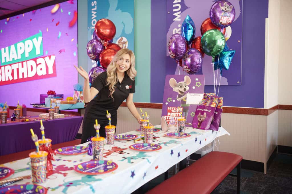 Chuck&nbsp;E.&nbsp;Cheese team member setting up a birthday party table with balloons and party favors.
