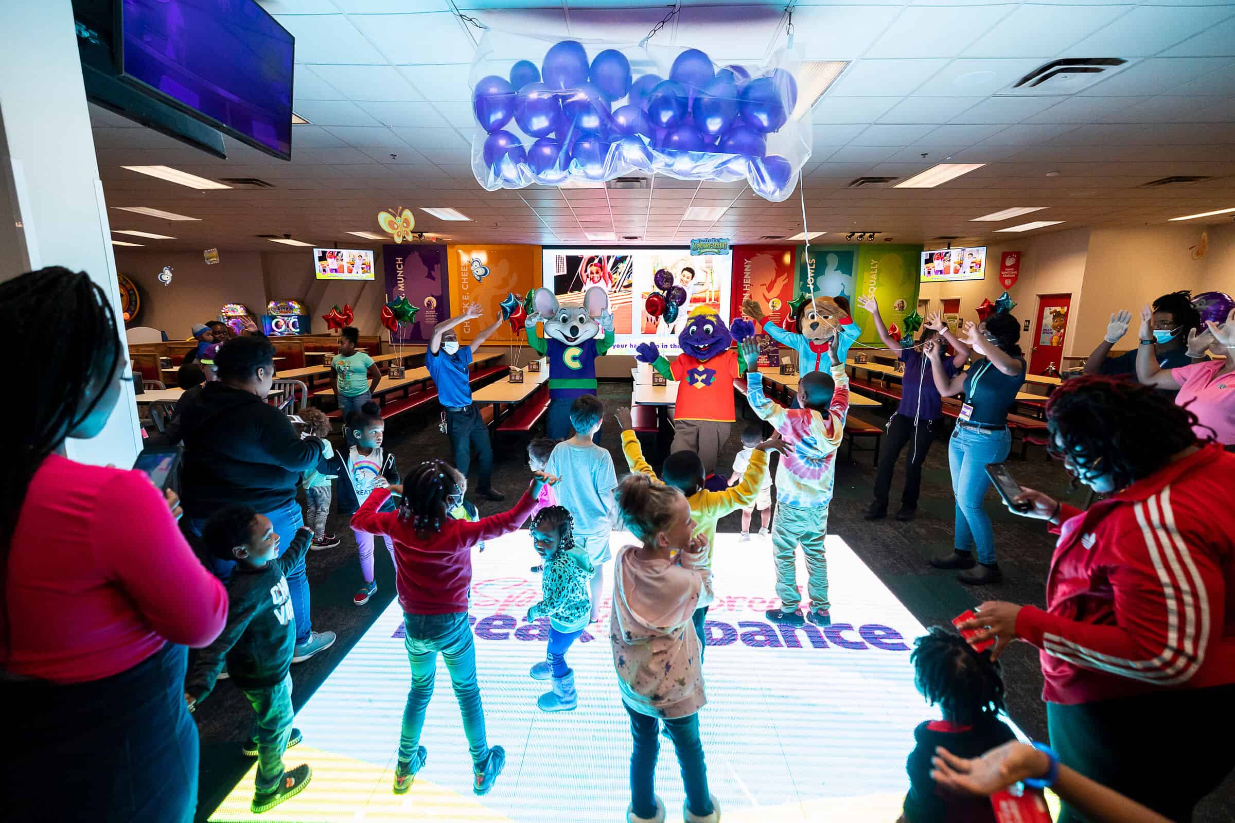 Kids and adults dancing with Chuck E. Cheese, Munch, and Jasper on the light-up dance floor at a Chuck E. Cheese party.