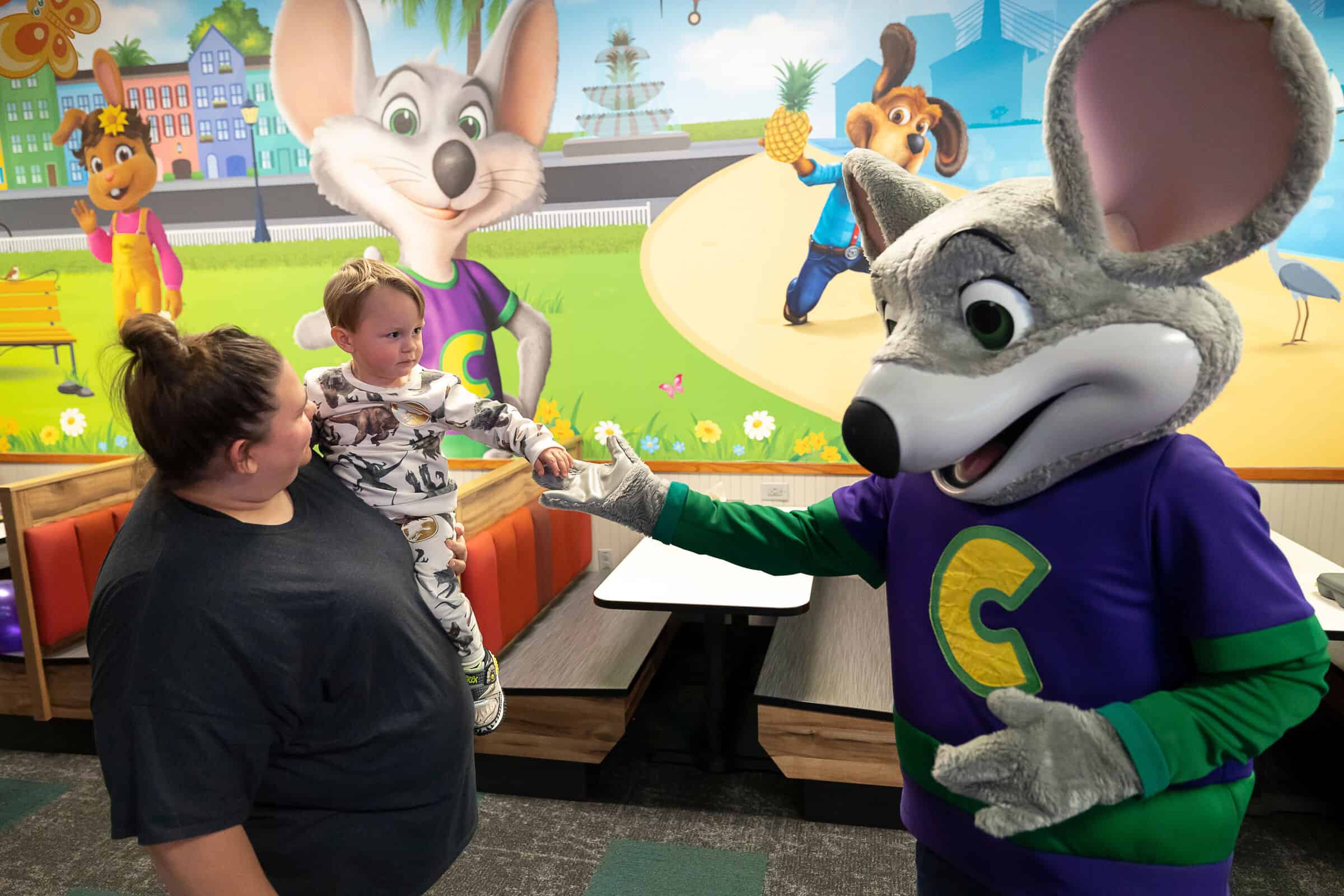 Toddler held by an adult reaching toward Chuck E. Cheese in excitement at a Chuck E. Cheese location