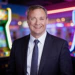 Smiling man in a suit in front of a colorful arcade, representing CEC Entertainment leadership.