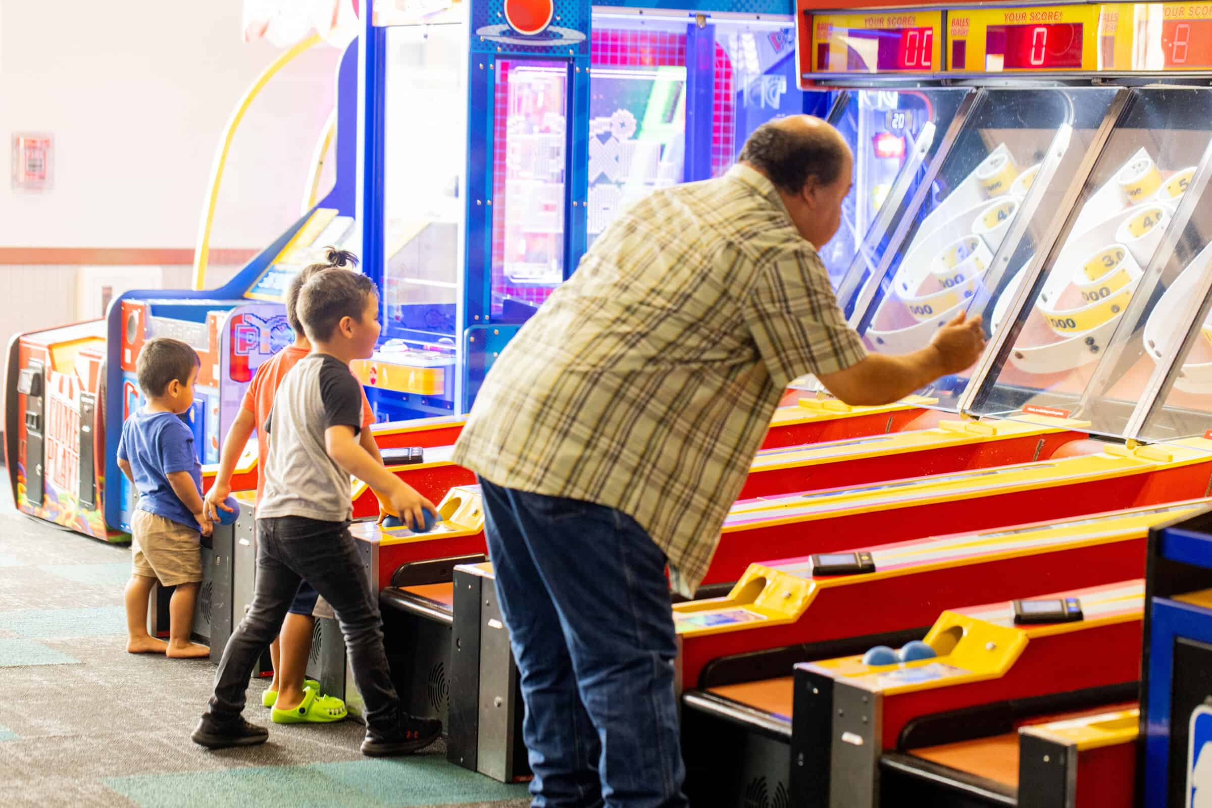 Grandfather and two young boys playing arcade games together at Chuck E. Cheese