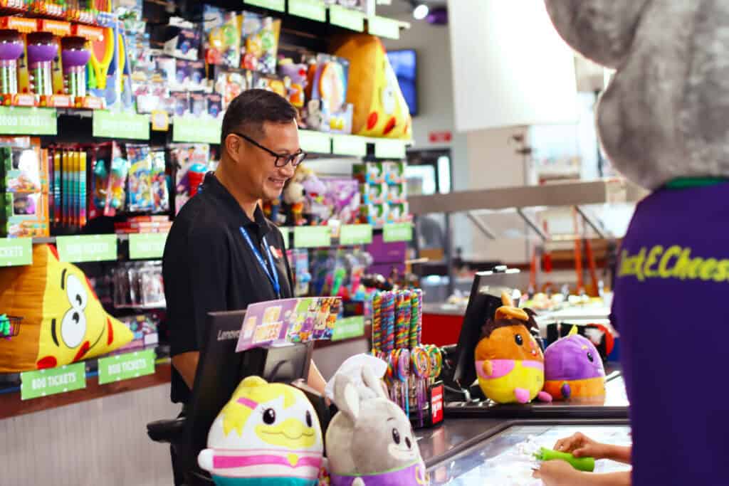 Chuck E. Cheese team member helping a child redeem tickets for prizes at the prize counter.