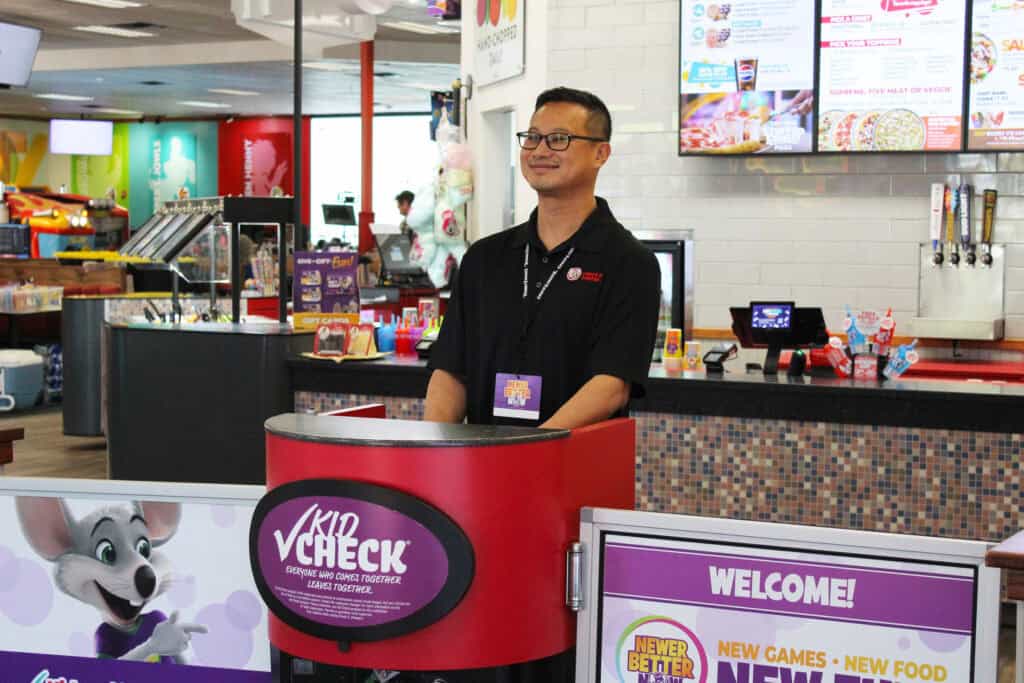 Chuck E. Cheese team member smiling at the Kid Check station, ensuring guest safety at the entrance.