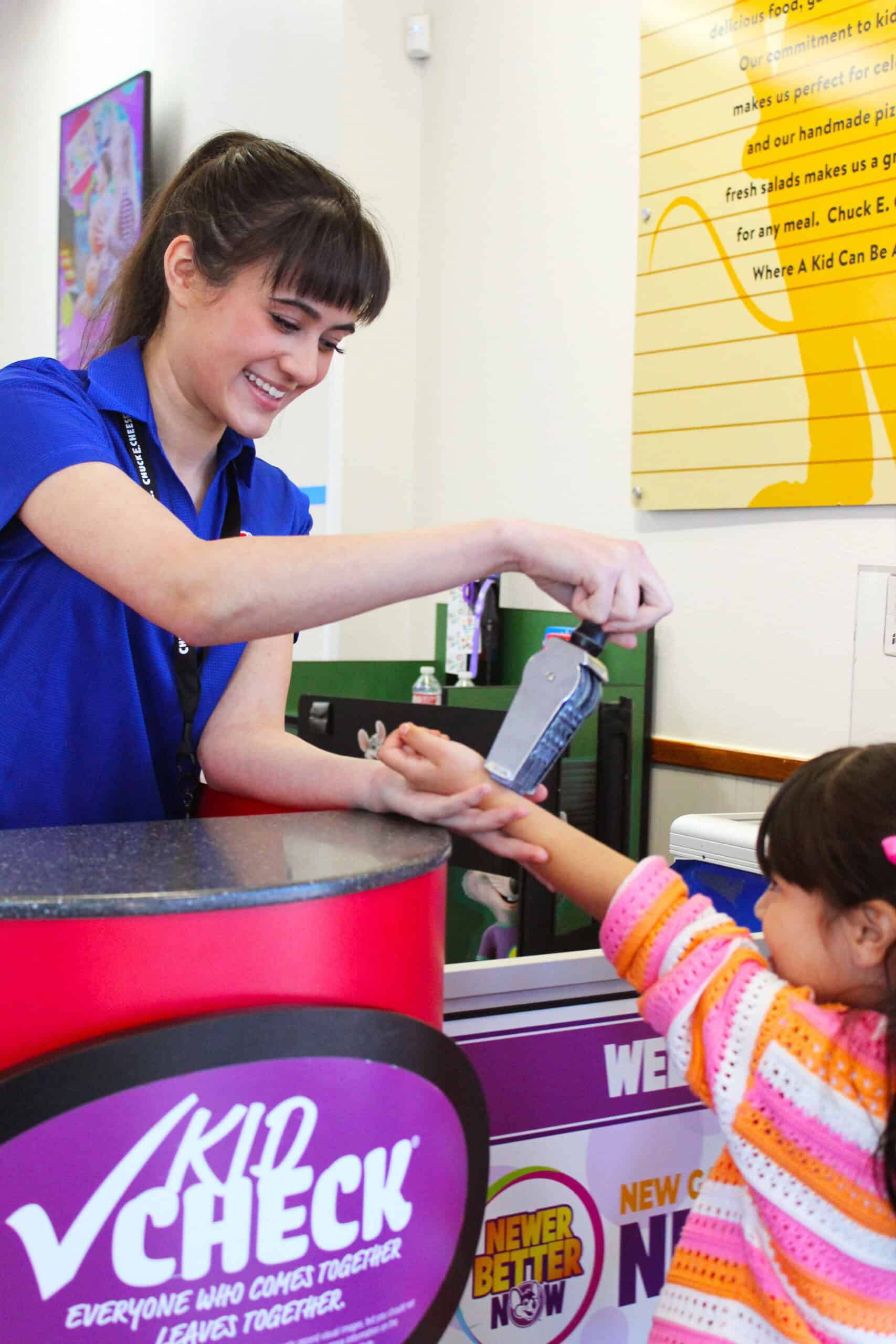 Chuck E. Cheese team member applying a Kid Check stamp to a child's hand at entrance