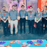 Chuck E. Cheese team, mostly young adults, stand in a party room with character posters and vibrant carpet at the family fun center.